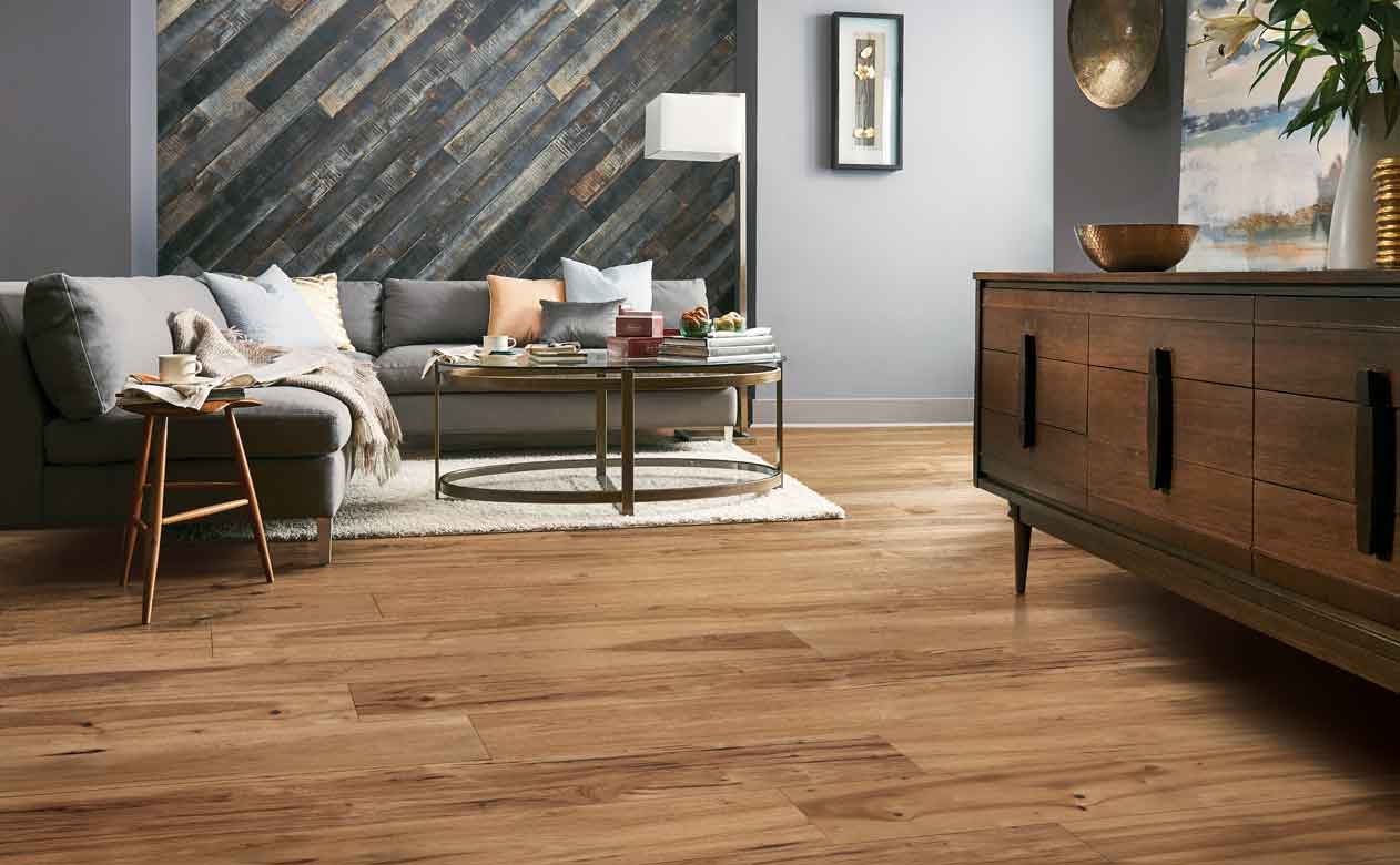 rustic hardwood flooring and wood paneling on accent wall in living area with large gray sectional